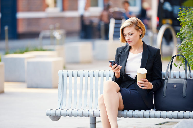 Women drinking coffee on bench with tote bag next to her