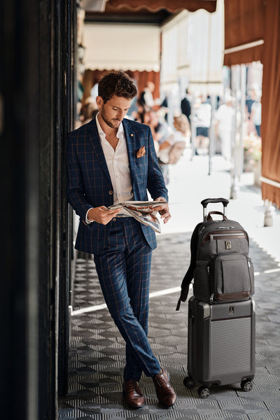 Man in a suit on his phone with a Platinum Elite hardside carry on suitcase and a platinum elite business backpack in grey